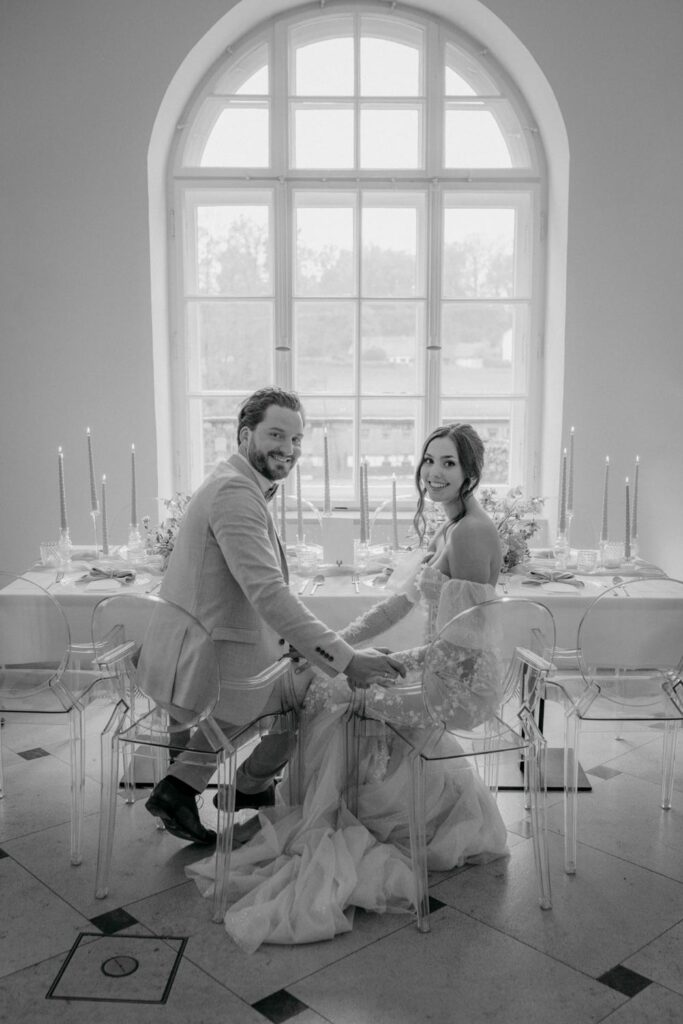 Brautpaar bei Hochzeitstisch vor großem Fenster