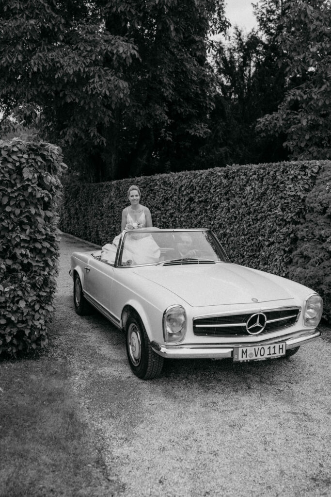 Braut in einem klassischen Mercedes Cabrio fährt.