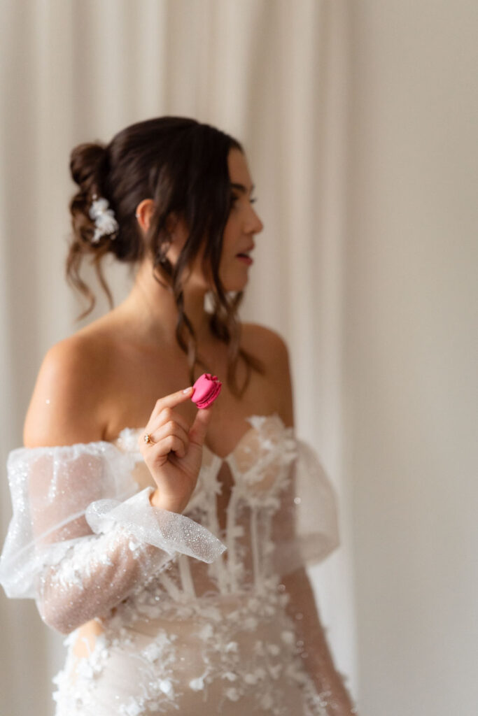 Braut in Spitzenkleid hält rosa Macaron fest