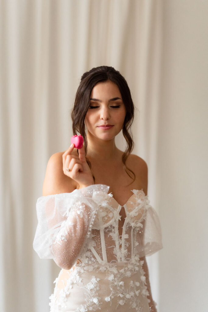 Braut in Spitzenkleid hält rosa Macaron genießen
